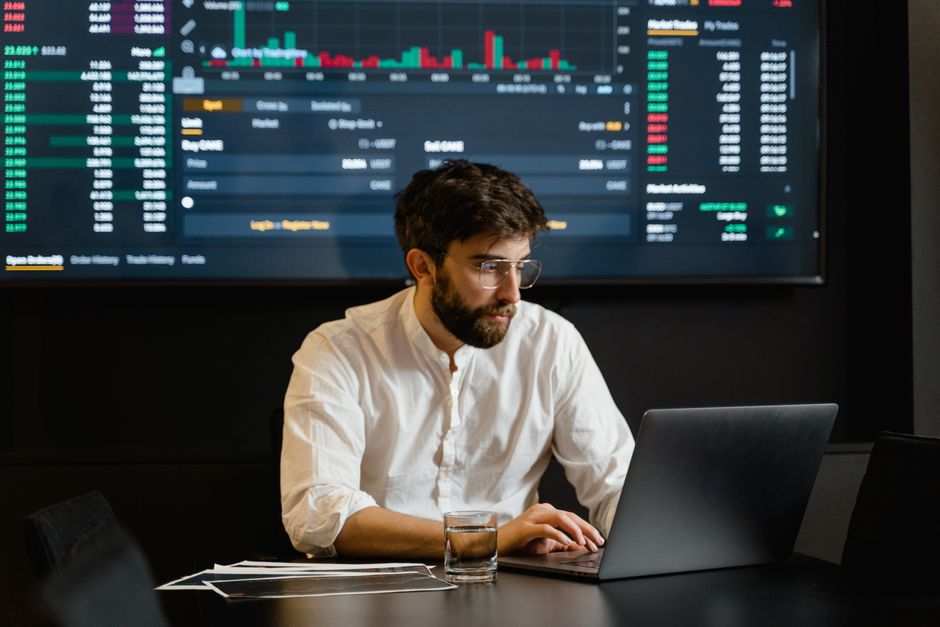 Professional analyzing stock market trends using laptop and digital display in modern office.